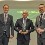 Trzech mężczyzn w garniturach pozuje do zdjęcia, jeden z nich trzyma statuetkę.