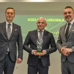 Trzech mężczyzn w garniturach pozuje do zdjęcia, jeden z nich trzyma statuetkę.